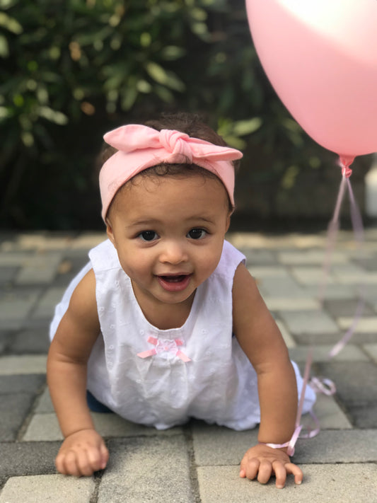 Baby with a headband on crawling next to a balloon